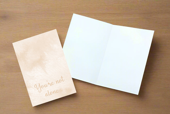 Two greeting cards on a wooden surface, one with 'You're not alone' text.