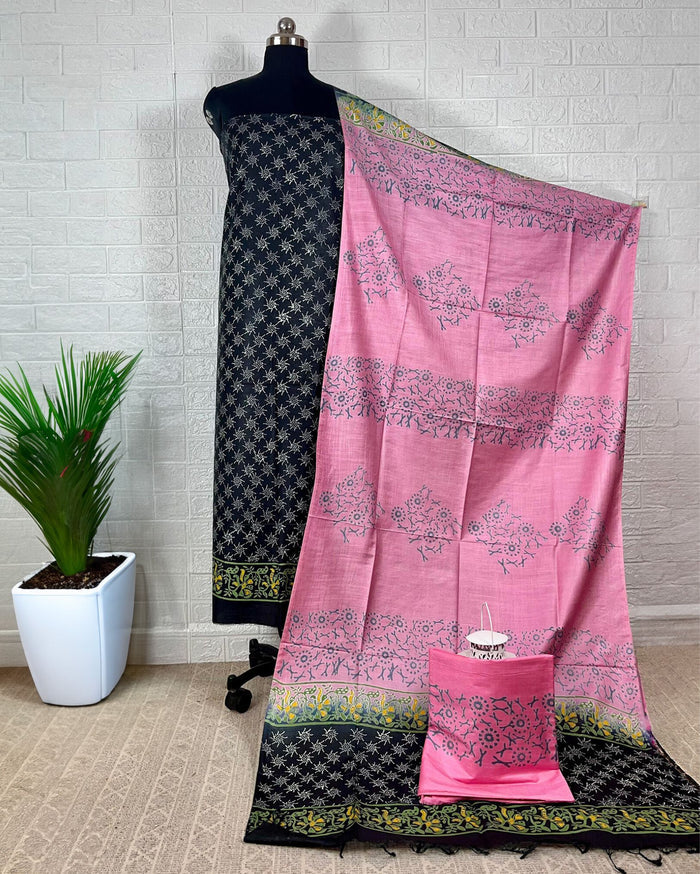 Black Katan silk suit set hand block printed with yellow and white geometric starburst motifs, paired with a contrast pink dupatta printed in floral clusters with banded edges.