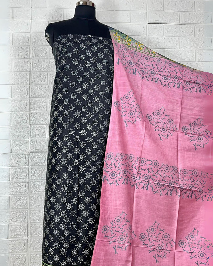 Black Katan silk suit set hand block printed with yellow and white geometric starburst motifs, paired with a contrast pink dupatta printed in floral clusters with banded edges.