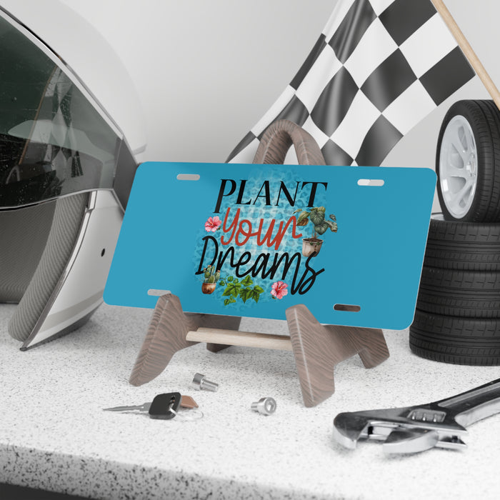 Blue license plate with 'Plant Your Dreams' text on a stand, surrounded by car parts and tools.