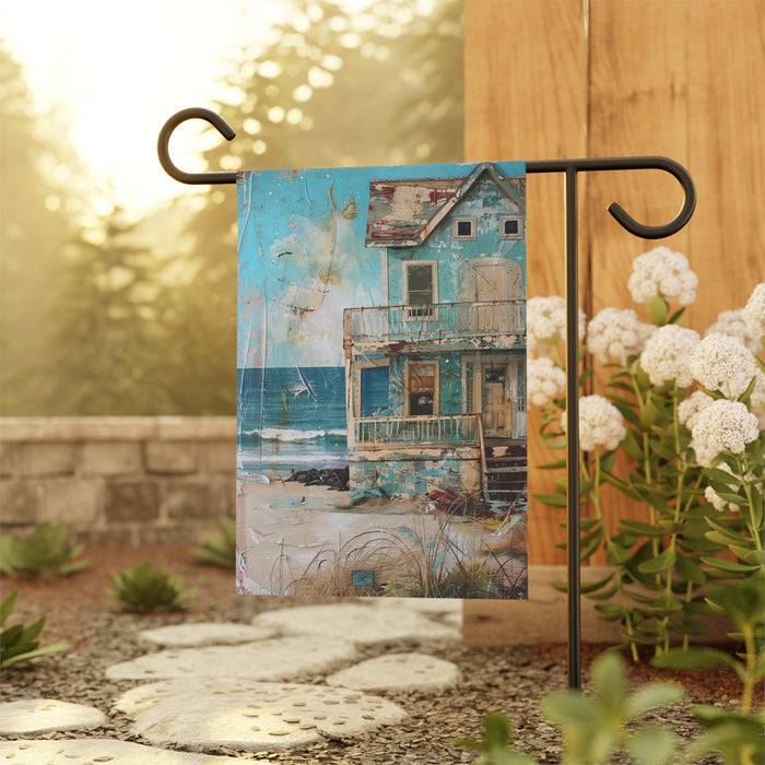 Decorative garden flag with a collage design of a house and landscape, attached to a stand outdoors.