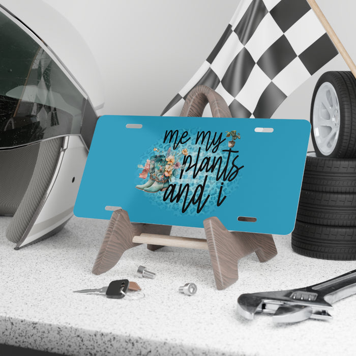 Blue license plate with 'me my plants and i' text and plant illustration on a stand, with car parts in the background.