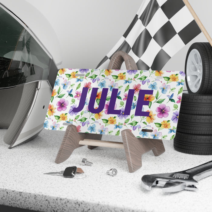 Decorative license plate with 'JULIE' and floral design on a stand, with car parts in the background.