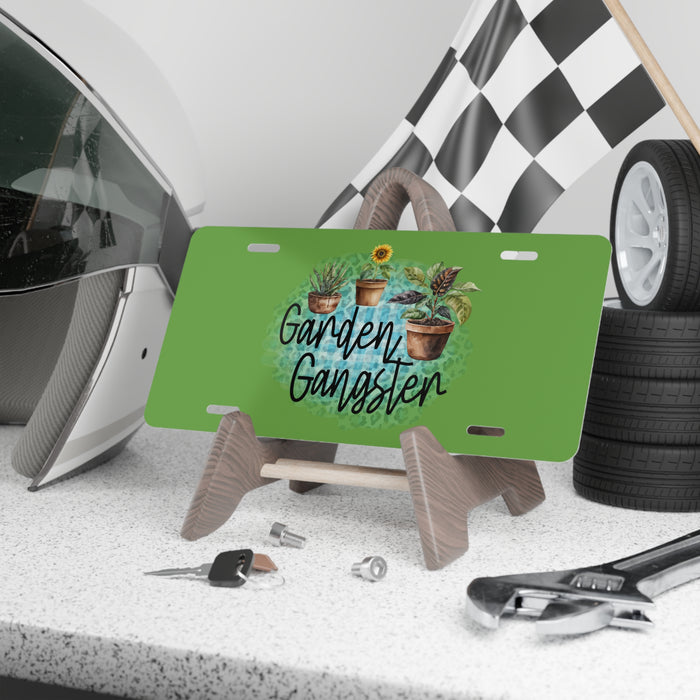 Green license plate with 'Garden Gangster' design on a stand, surrounded by tools and a helmet.