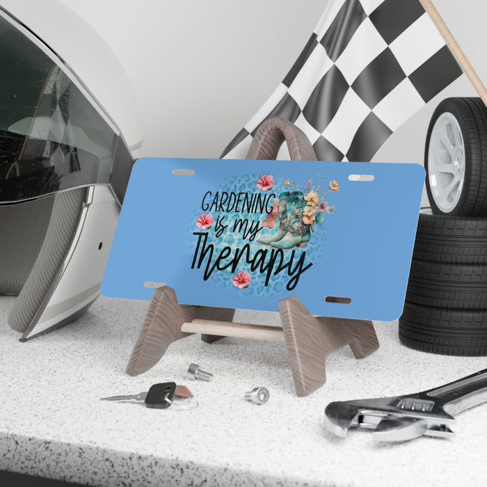 Blue license plate with 'Gardening is my Therapy' text and floral design on a stand, surrounded by tools and tires.