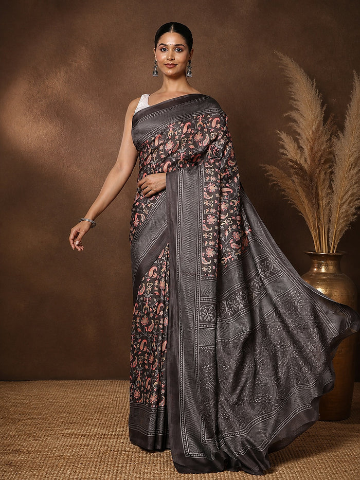 Charcoal grey printed saree with a floral and paisley print in pink, mustard and green, framed by a wide decorative border.