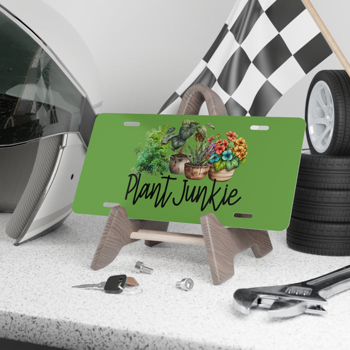 Green license plate with 'Plant Junkie' design on a stand, surrounded by car parts and tools.