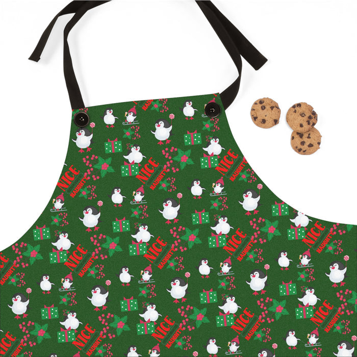 Green apron with Christmas-themed design featuring penguins and text, accompanied by cookies on a white background.