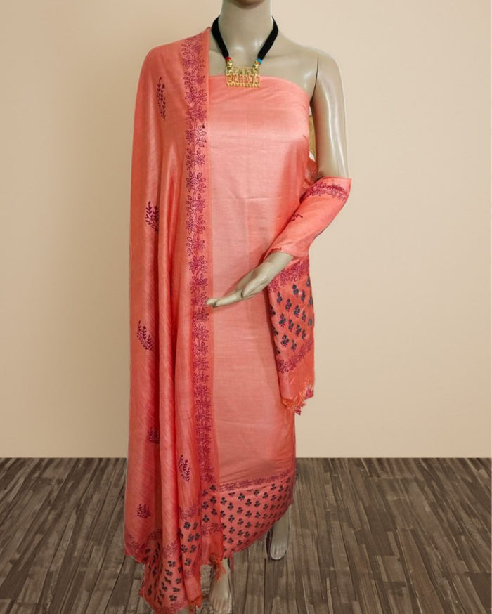 Solid peach katan silk unstitched suit set with a hand block printed dark plum floral panel down one edge of the dupatta and a patterned band at its base.