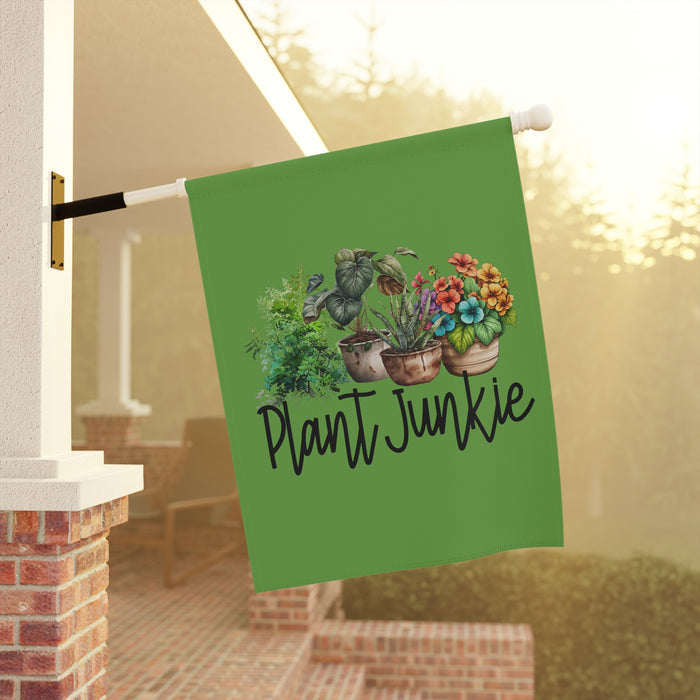 Green garden flag with plant-themed design and 'Plant Junkie' text, hanging outdoors.