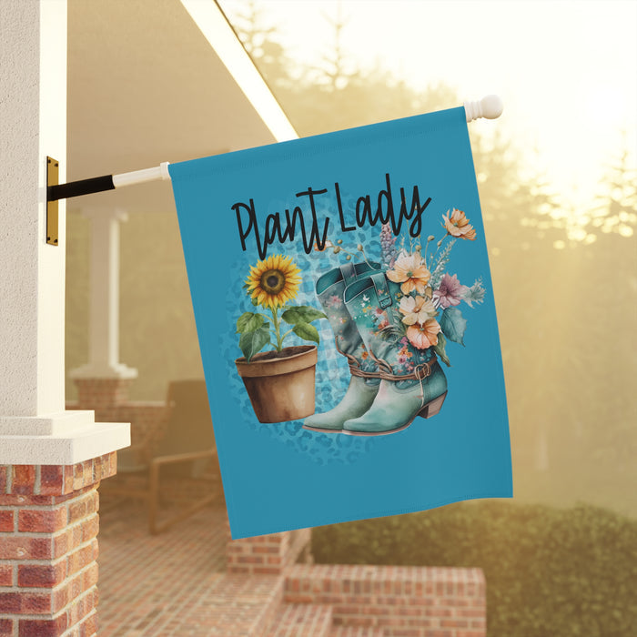 Decorative garden flag with 'Plant Lady' text, boots, sunflower, and flowers on a blue background, hanging outdoors.