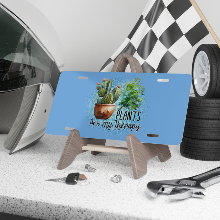 Blue license plate with plant design and text, placed on a stand with tools and tires in the background.
