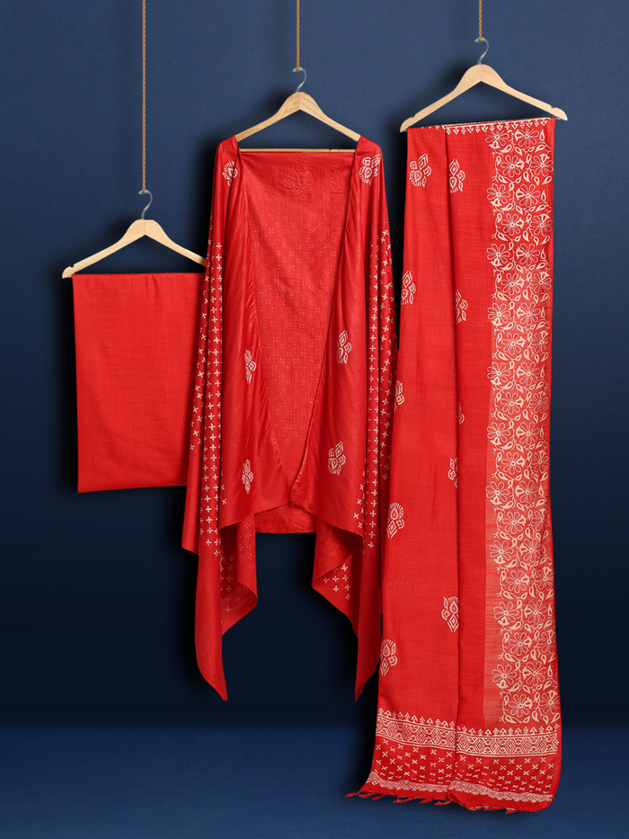 Unstitched red Katan silk suit set block printed with scattered cream and white floral and geometric motifs, a plain unprinted bottom, and a dupatta with a wide floral panel border and a geometric band along the lower edge.