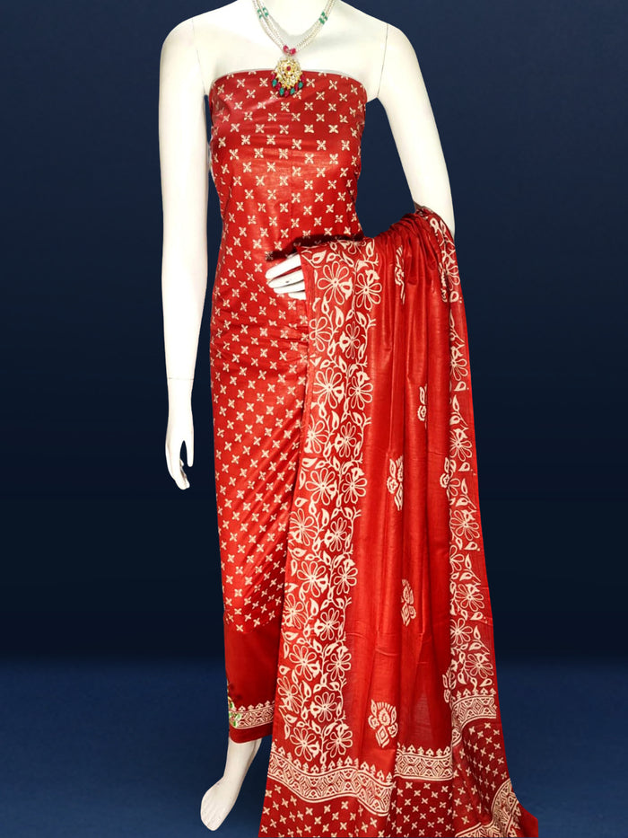 Unstitched red Katan silk suit set block printed with scattered cream and white floral and geometric motifs, a plain unprinted bottom, and a dupatta with a wide floral panel border and a geometric band along the lower edge.