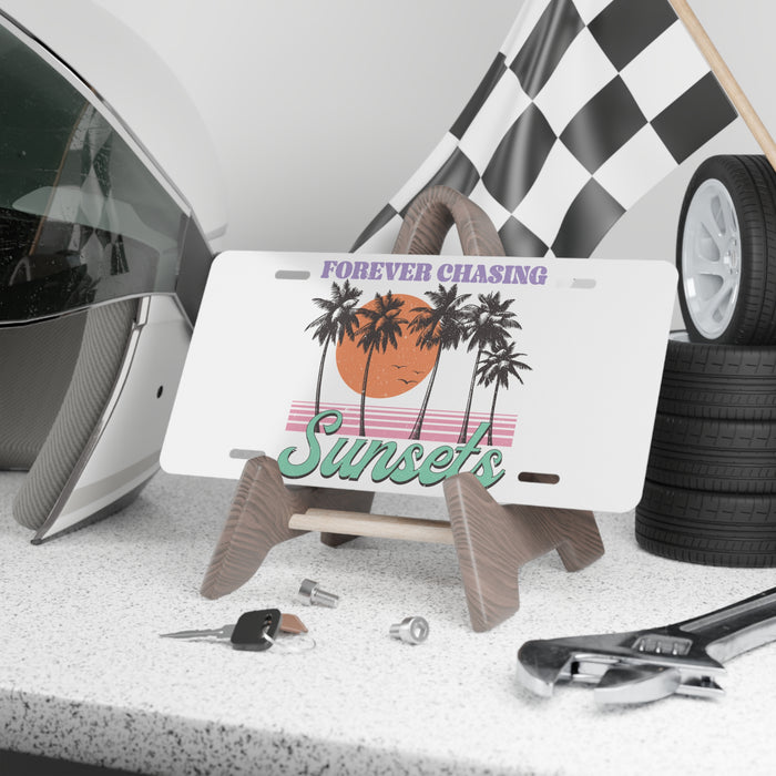 License plate with 'Forever Chasing Sunsets' design on a stand, surrounded by car parts and tools.