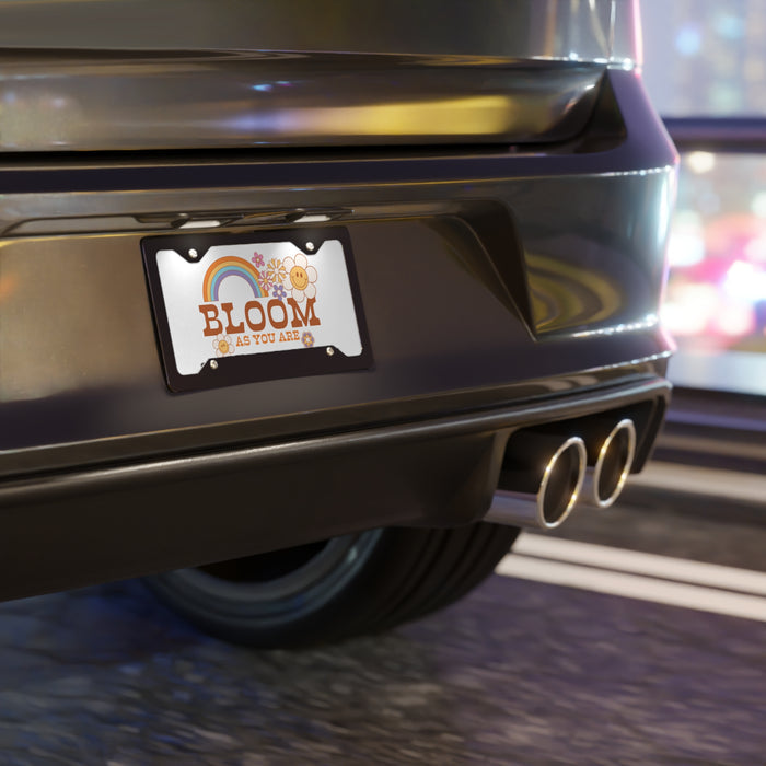 Car license plate with 'BLOOM' text and rainbow design on a blurred street background