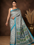 White Kashmiri Silk printed saree with an all-over paisley, floral and vine print in blue and green, a wide blue-and-green pallu panel and a narrow teal-blue border.